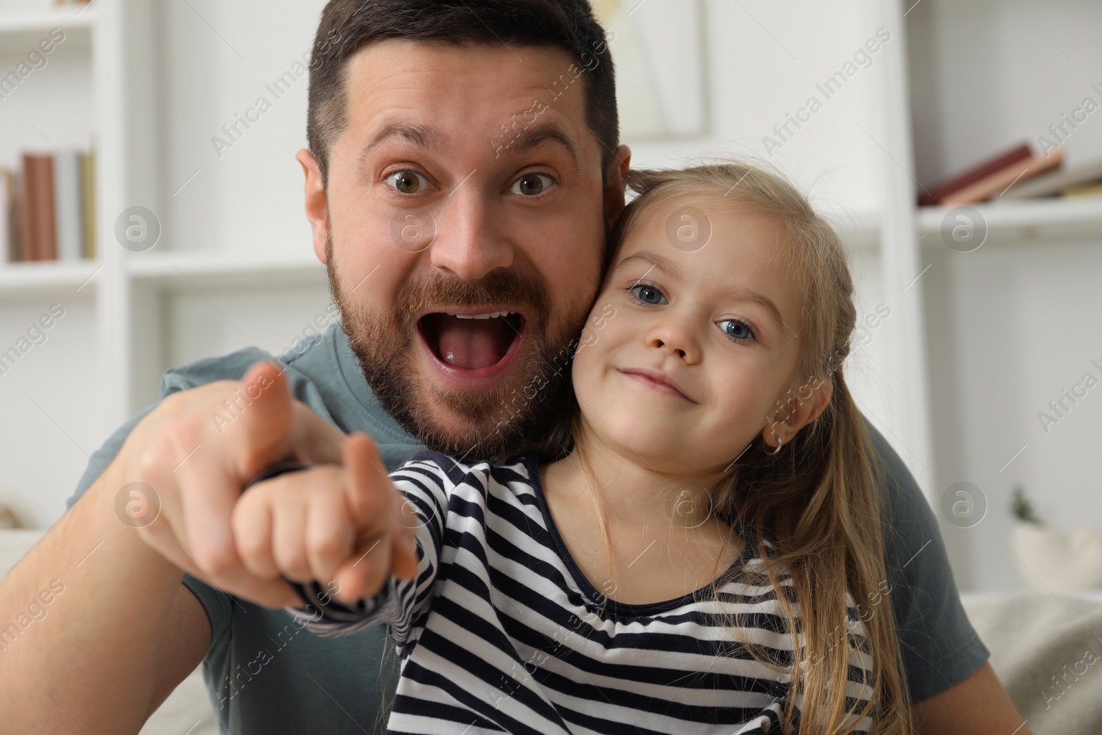 Photo of Surprised father and his cute little daughter looking at camera indoors