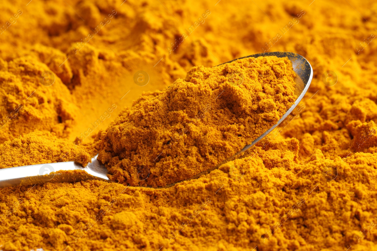 Photo of Turmeric powder in spoon on spice, closeup