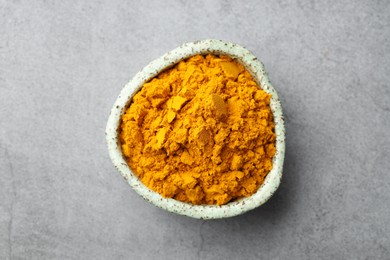 Photo of Turmeric powder in bowl on grey table, top view