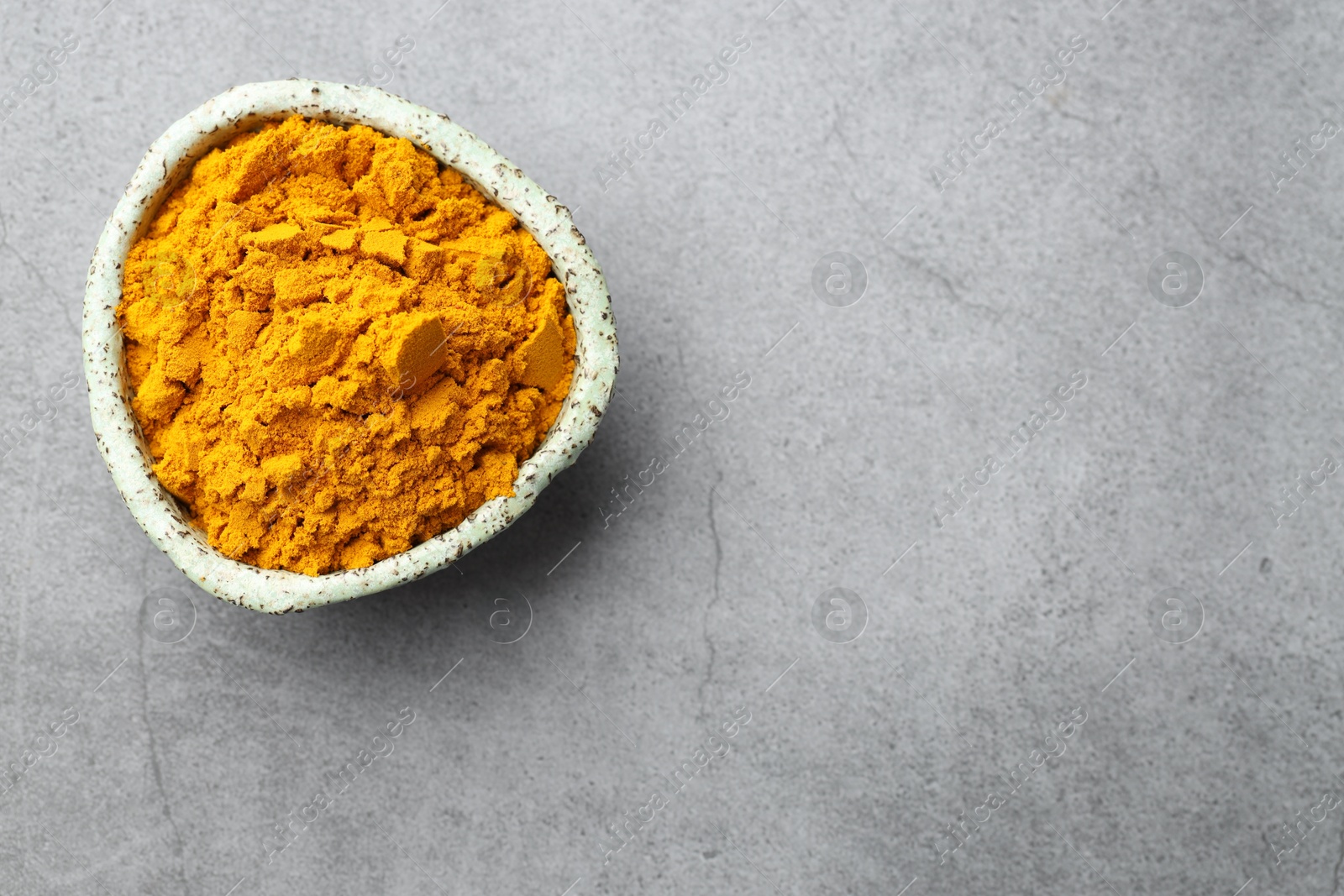 Photo of Turmeric powder in bowl on grey table, top view. Space for text