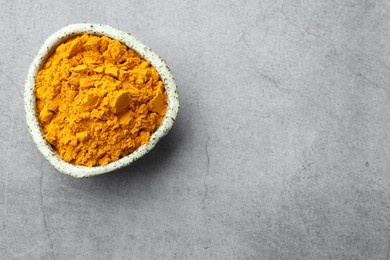 Photo of Turmeric powder in bowl on grey table, top view. Space for text