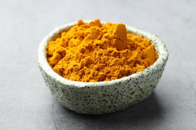 Photo of Turmeric powder in bowl on grey table, closeup