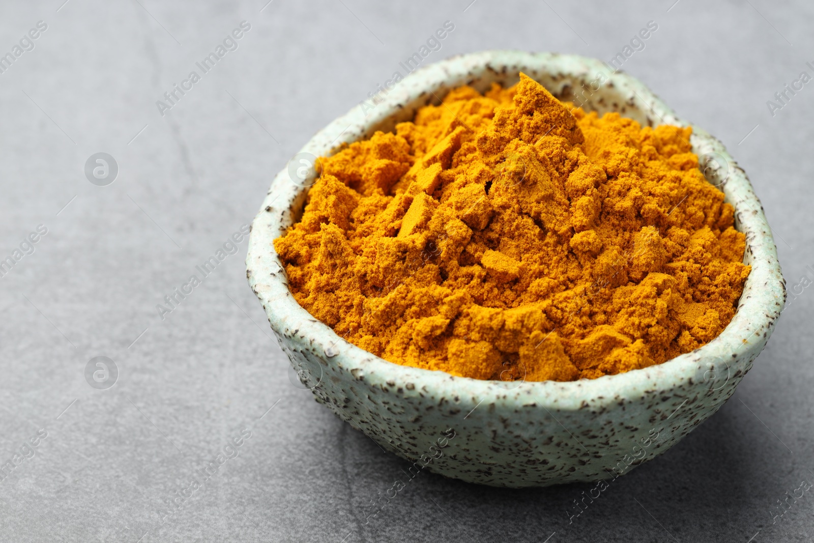 Photo of Turmeric powder in bowl on grey table, closeup. Space for text