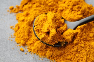 Photo of Turmeric powder and spoon on grey table, closeup