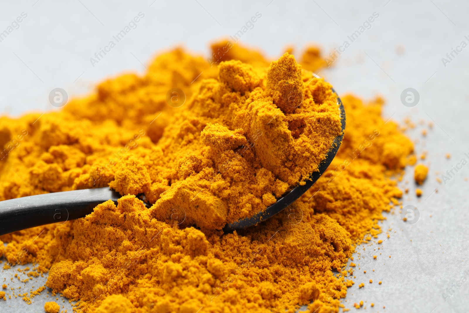 Photo of Turmeric powder and spoon on grey table, closeup