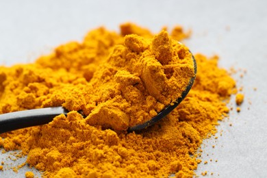 Photo of Turmeric powder and spoon on grey table, closeup