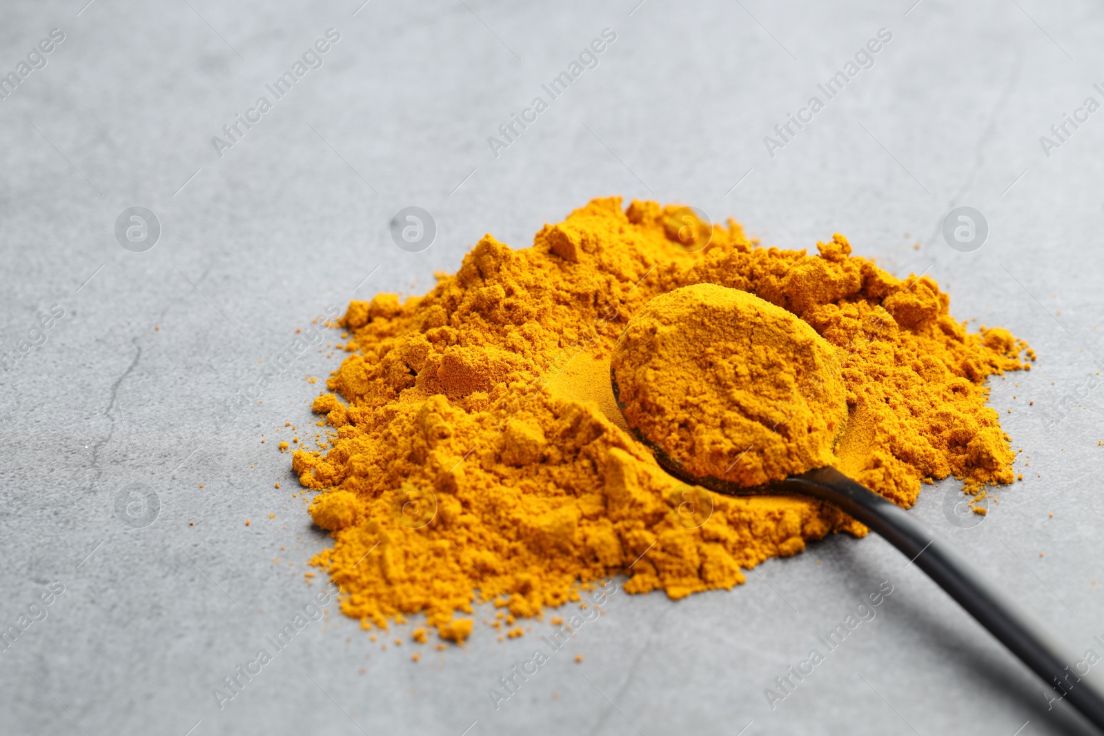 Photo of Turmeric powder and spoon on grey table, closeup. Space for text