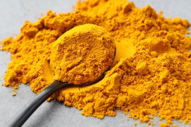 Photo of Turmeric powder and spoon on grey table, closeup