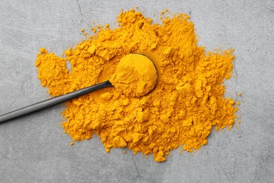 Photo of Turmeric powder and spoon on grey table, top view