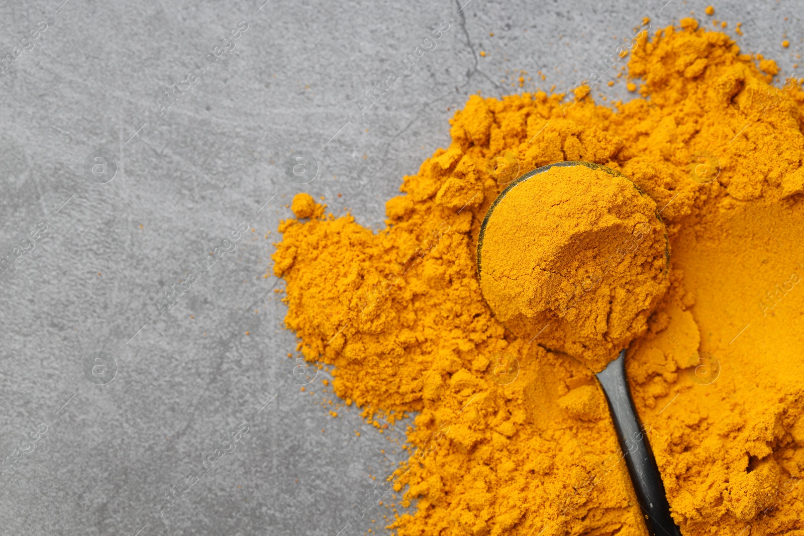 Photo of Turmeric powder and spoon on grey table, top view. Space for text