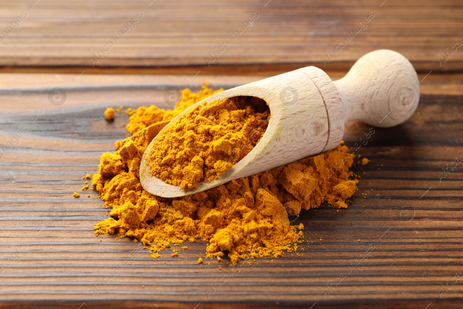 Photo of Turmeric powder in scoop on wooden table, closeup