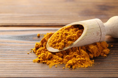 Photo of Turmeric powder in scoop on wooden table, closeup. Space for text