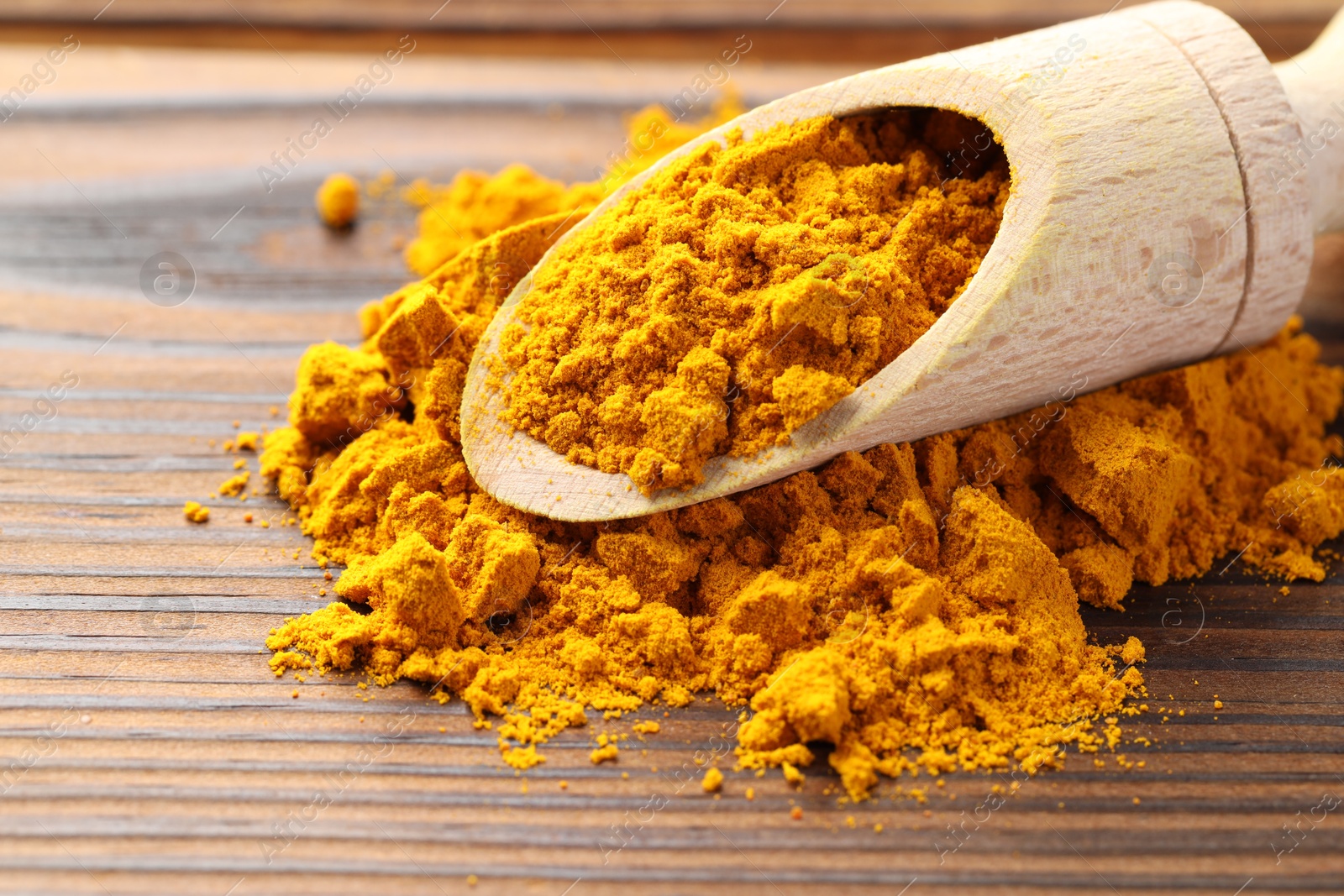 Photo of Turmeric powder in scoop on wooden table, closeup