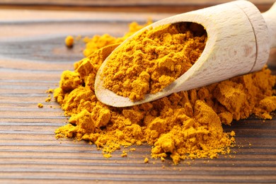 Photo of Turmeric powder in scoop on wooden table, closeup