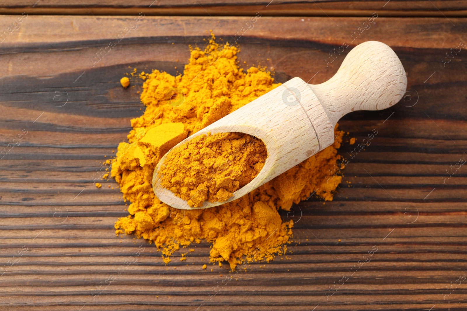 Photo of Turmeric powder in scoop on wooden table, top view