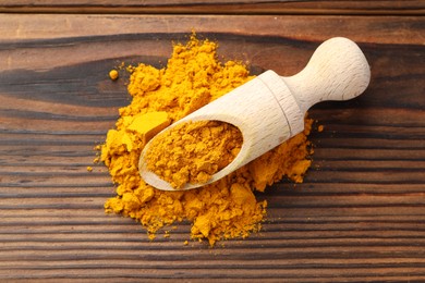 Turmeric powder in scoop on wooden table, top view