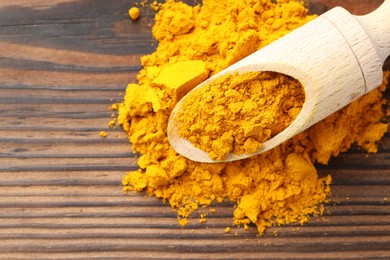 Photo of Turmeric powder in scoop on wooden table, top view. Space for text