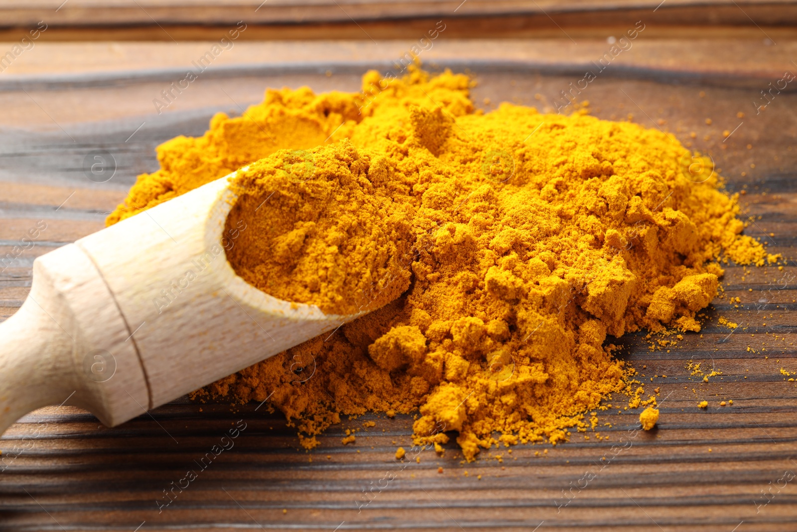 Photo of Turmeric powder in scoop on wooden table, closeup