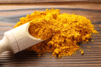 Photo of Turmeric powder in scoop on wooden table, closeup