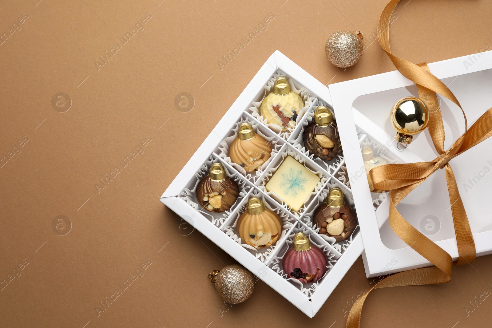 Photo of Delicious chocolate in shape of ornaments in open box and Christmas decor on beige background, flat lay. Space for text