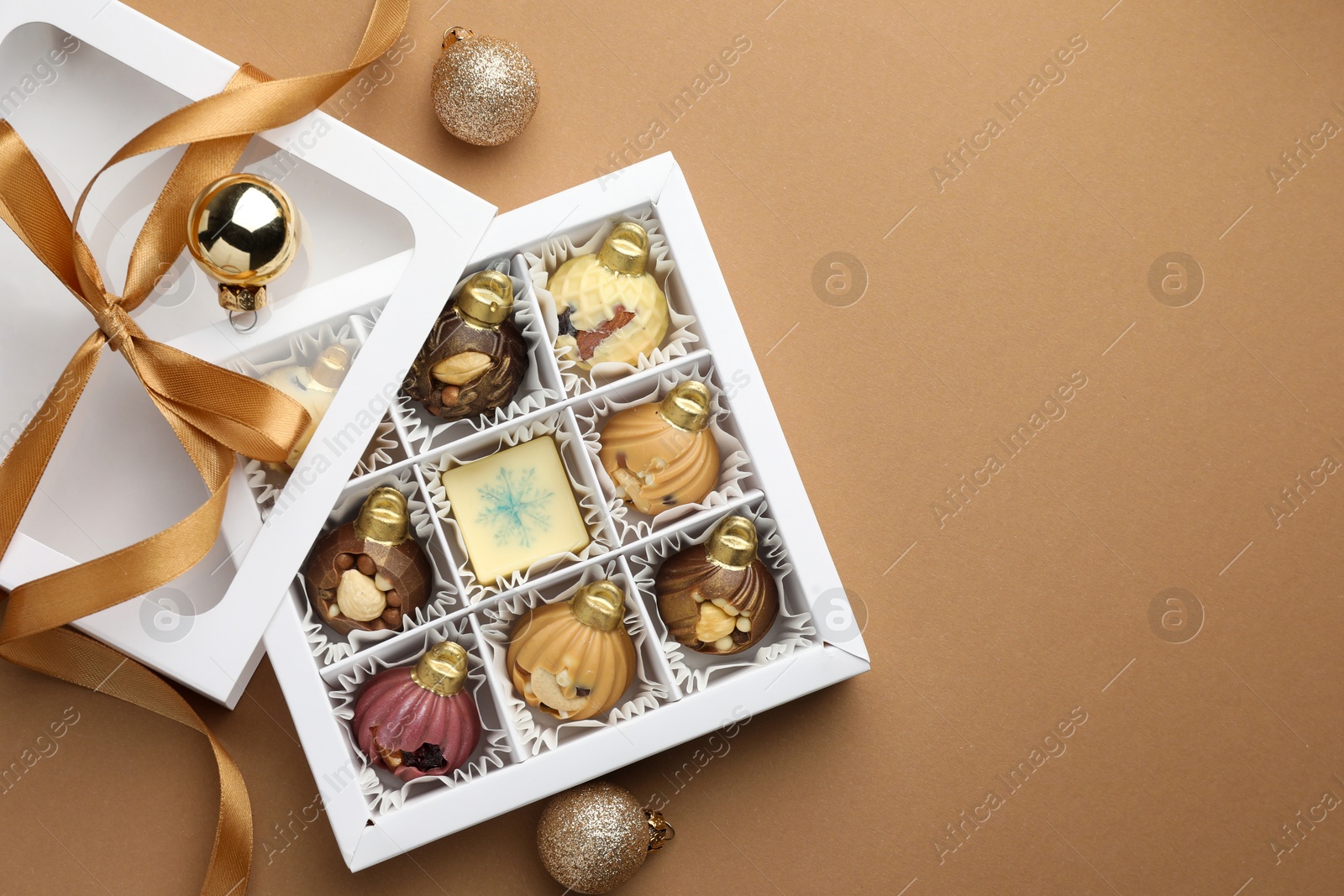 Photo of Delicious chocolate in shape of ornaments in open box and Christmas decor on beige background, flat lay. Space for text