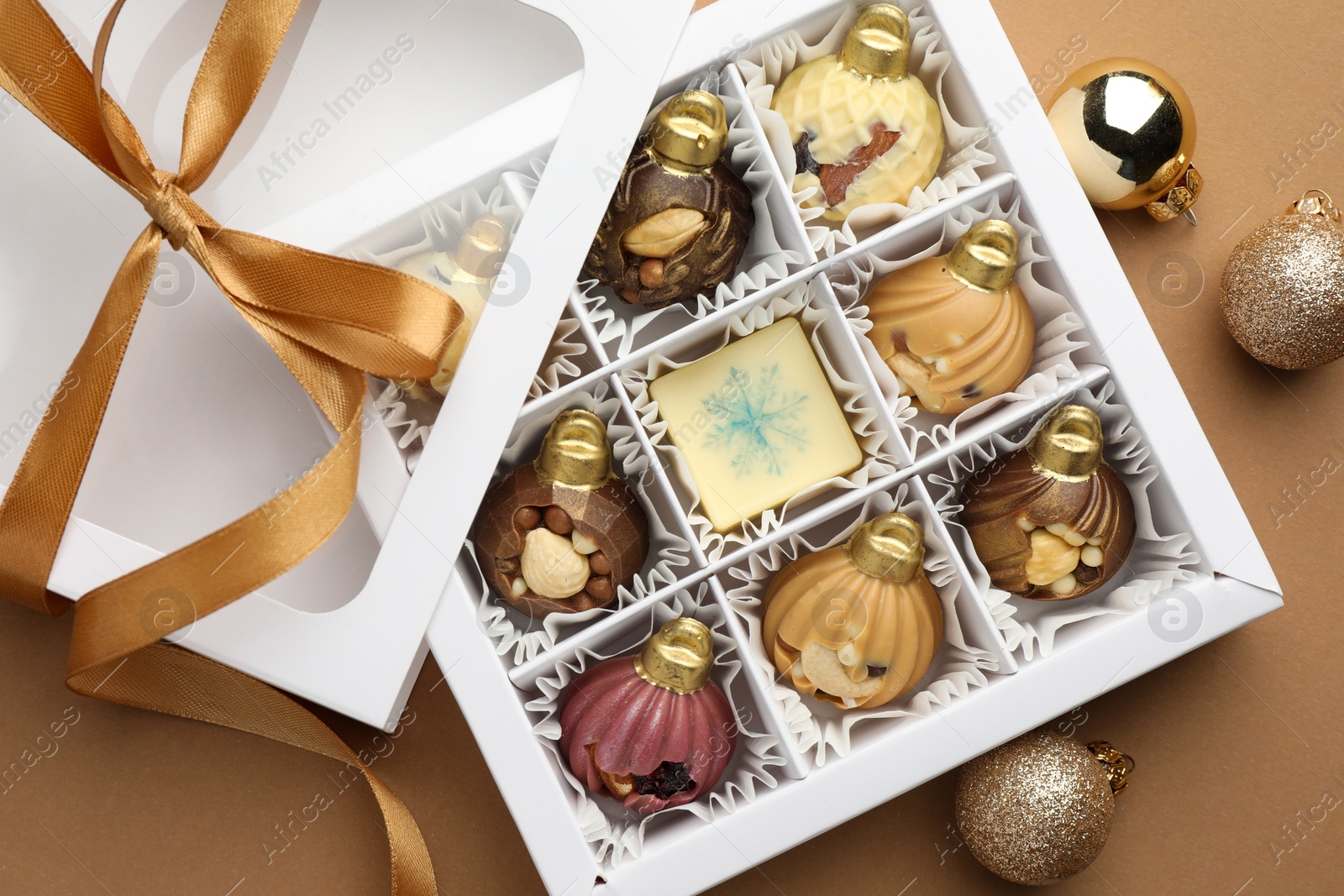 Photo of Delicious chocolate in shape of ornaments in open box and Christmas decor on beige background, flat lay