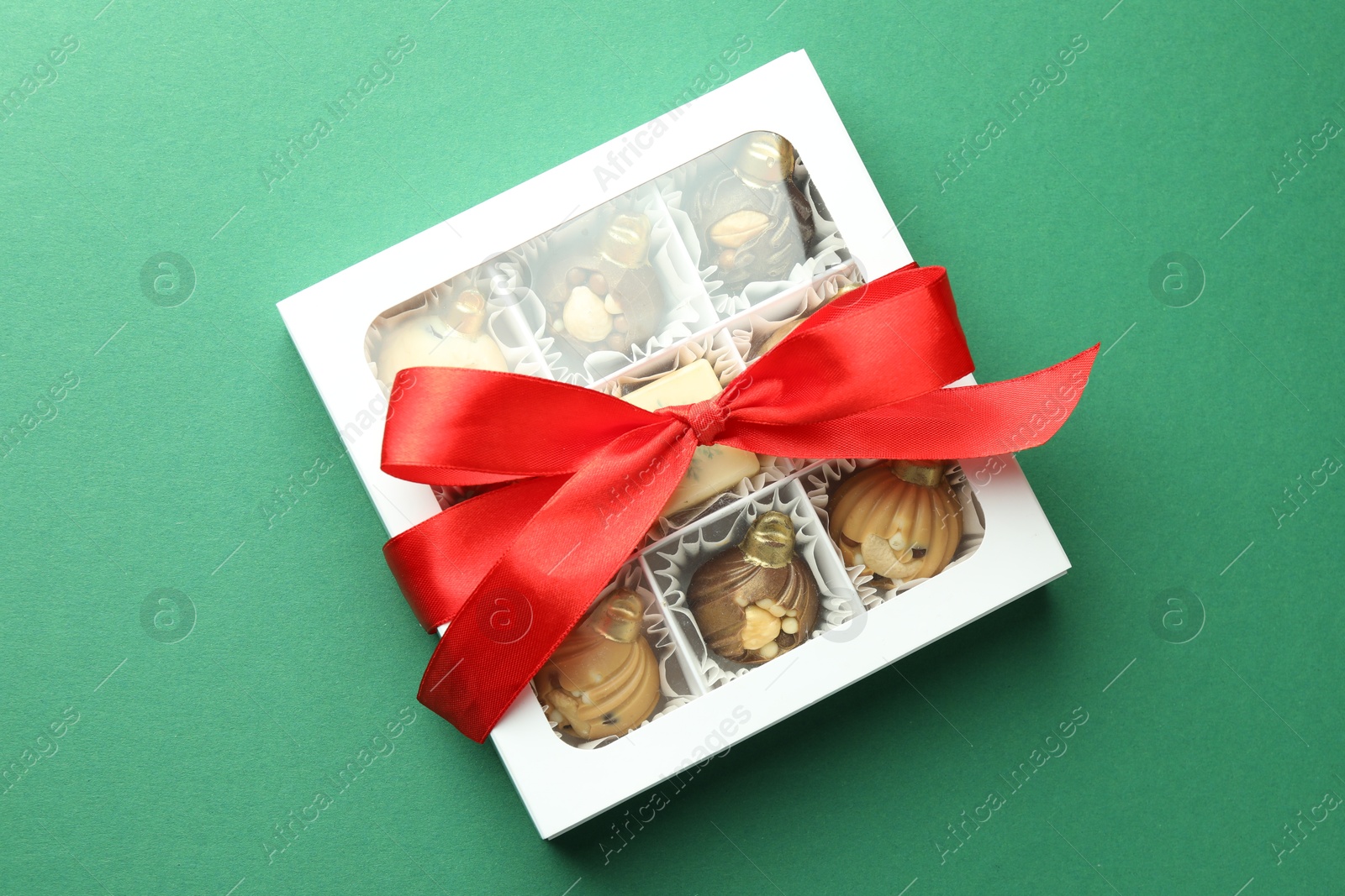 Photo of Box with tasty sweets in shape of baubles on green background, top view