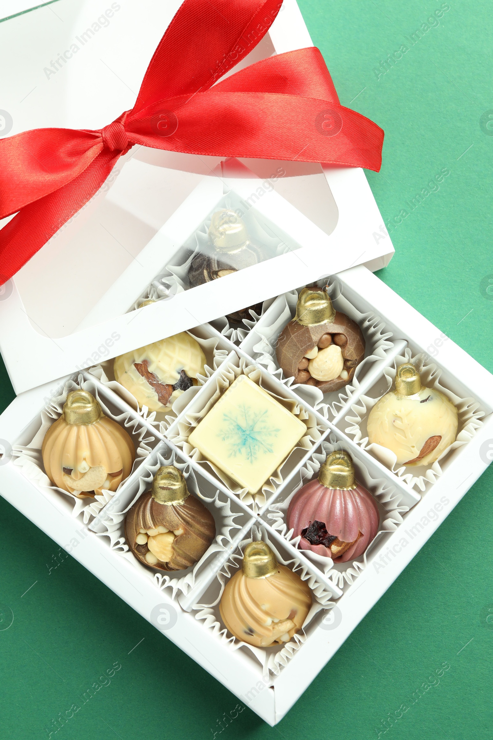 Photo of Box with tasty sweets in shape of baubles on green background, top view