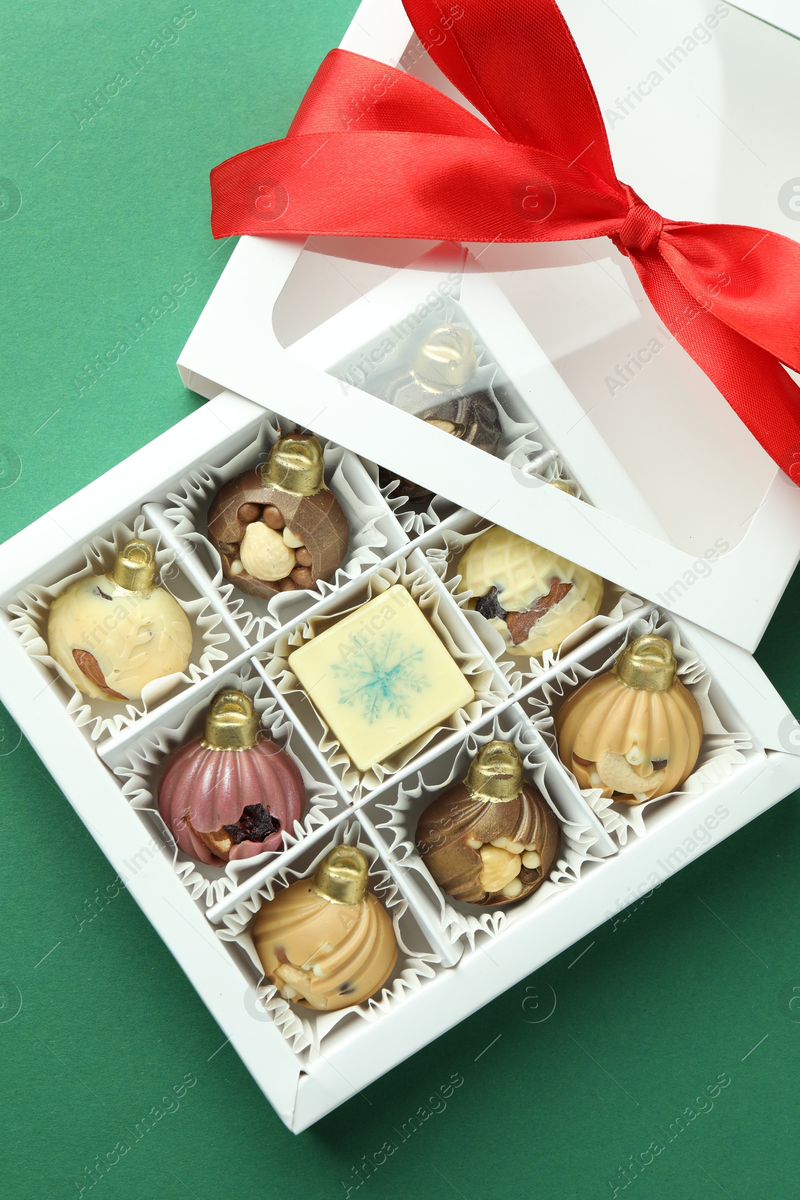 Photo of Box with tasty sweets in shape of baubles on green background, top view