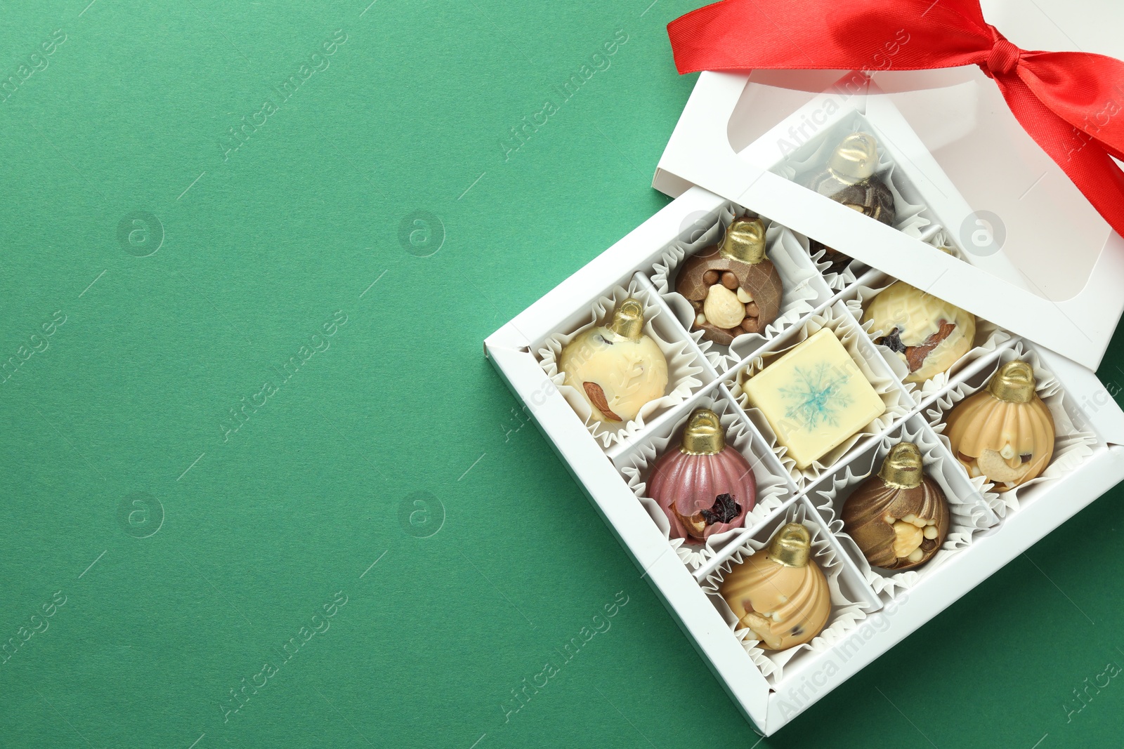 Photo of Box with tasty sweets in shape of baubles on green background, top view. Space for text