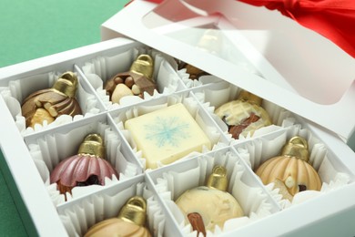 Photo of Box with tasty sweets in shape of baubles on green background, closeup