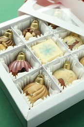 Photo of Box with tasty sweets in shape of baubles on green background, closeup