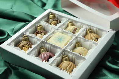 Photo of Box with tasty sweets in shape of baubles on green fabric background, closeup