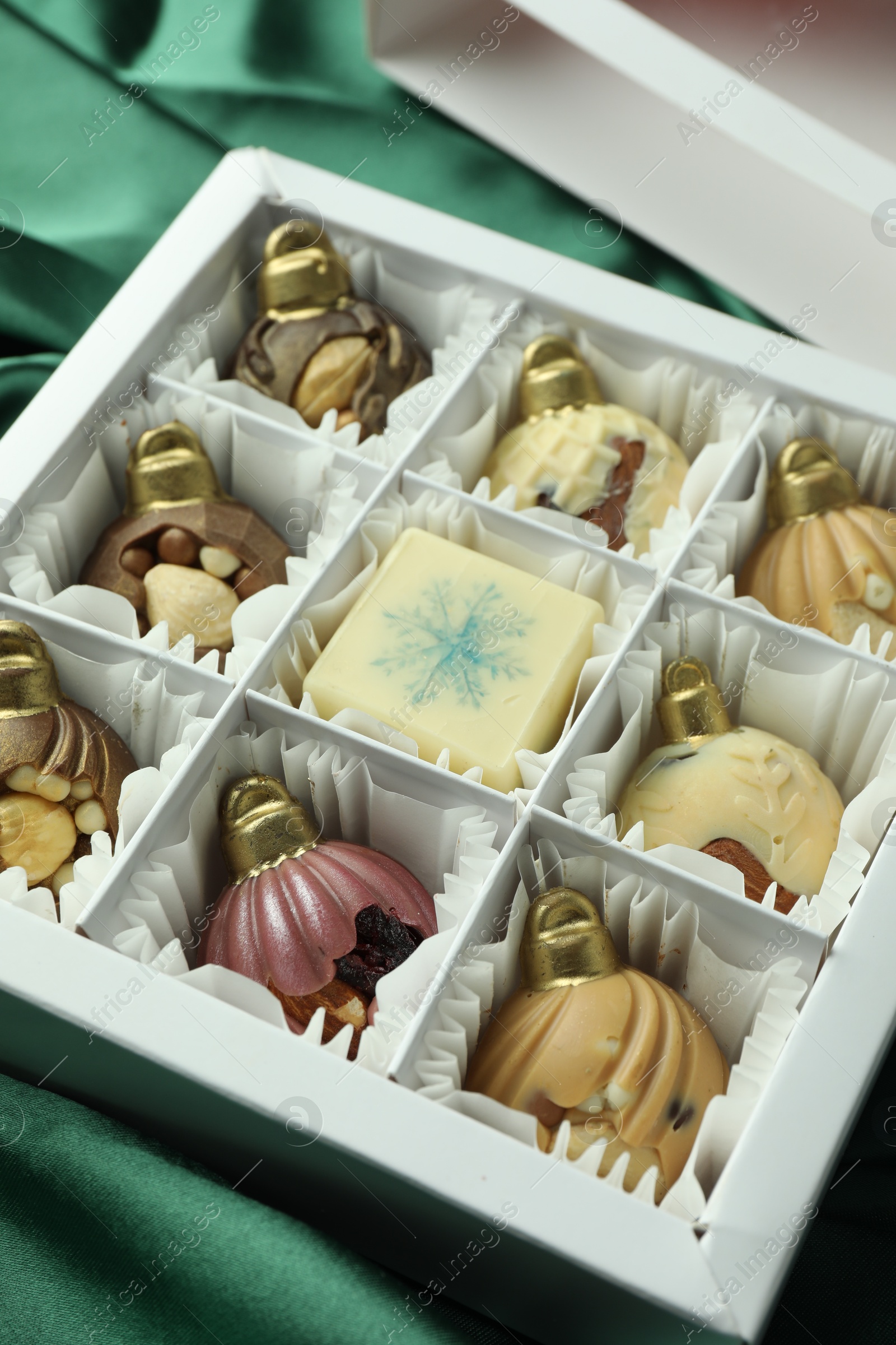 Photo of Box with tasty sweets in shape of baubles on green fabric background, closeup