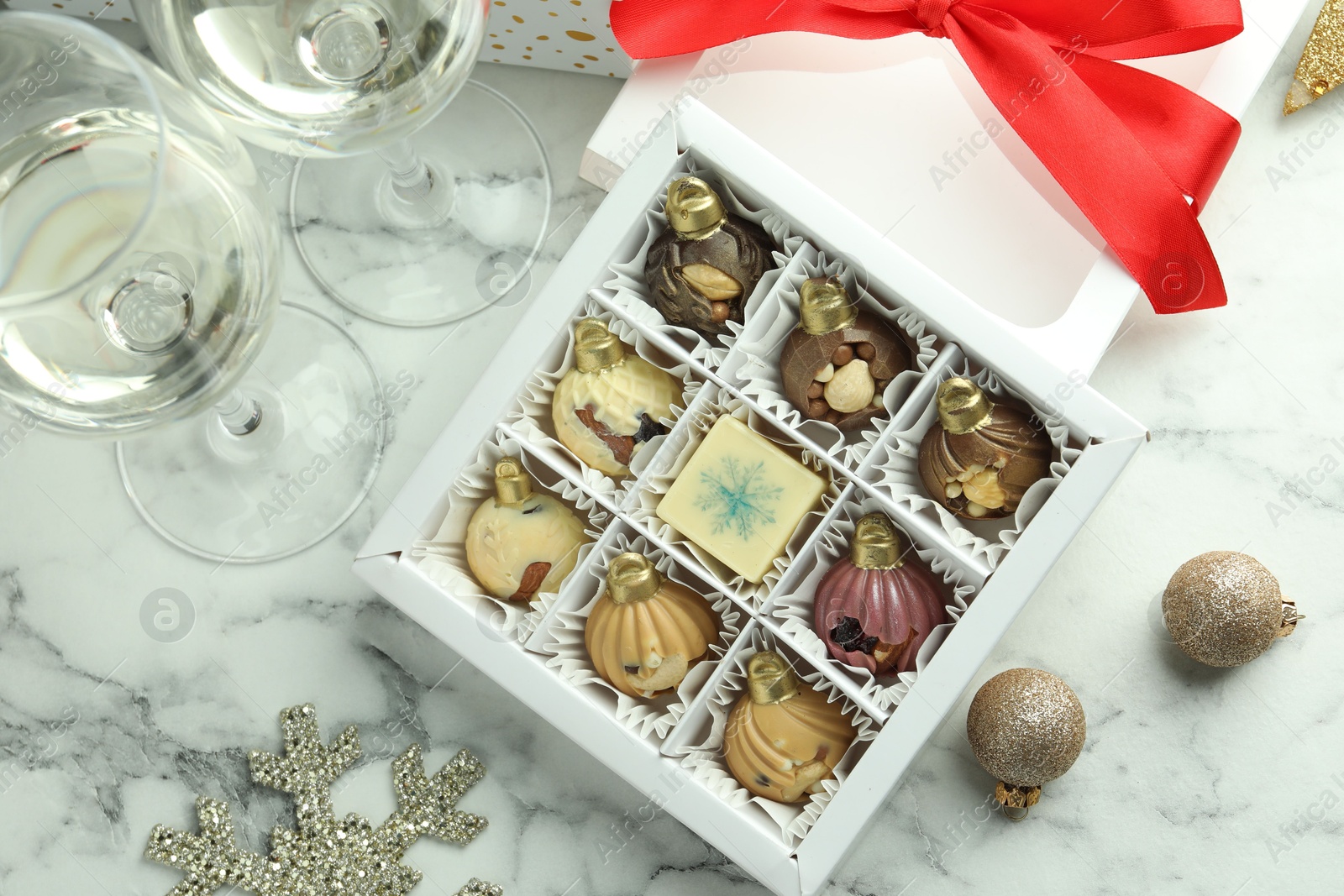 Photo of Box with tasty sweets in shape of baubles, wine and Christmas decor on white marble background, flat lay