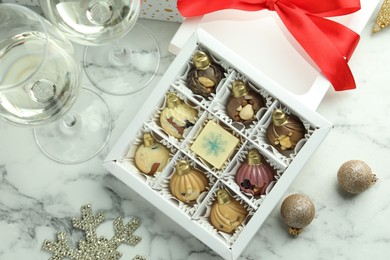 Photo of Box with tasty sweets in shape of baubles, wine and Christmas decor on white marble background, flat lay