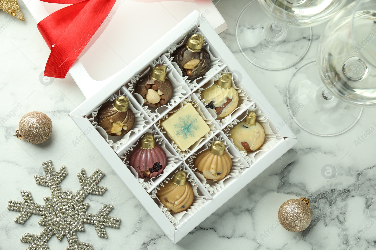 Photo of Box with tasty sweets in shape of baubles, wine and Christmas decor on white marble background, flat lay