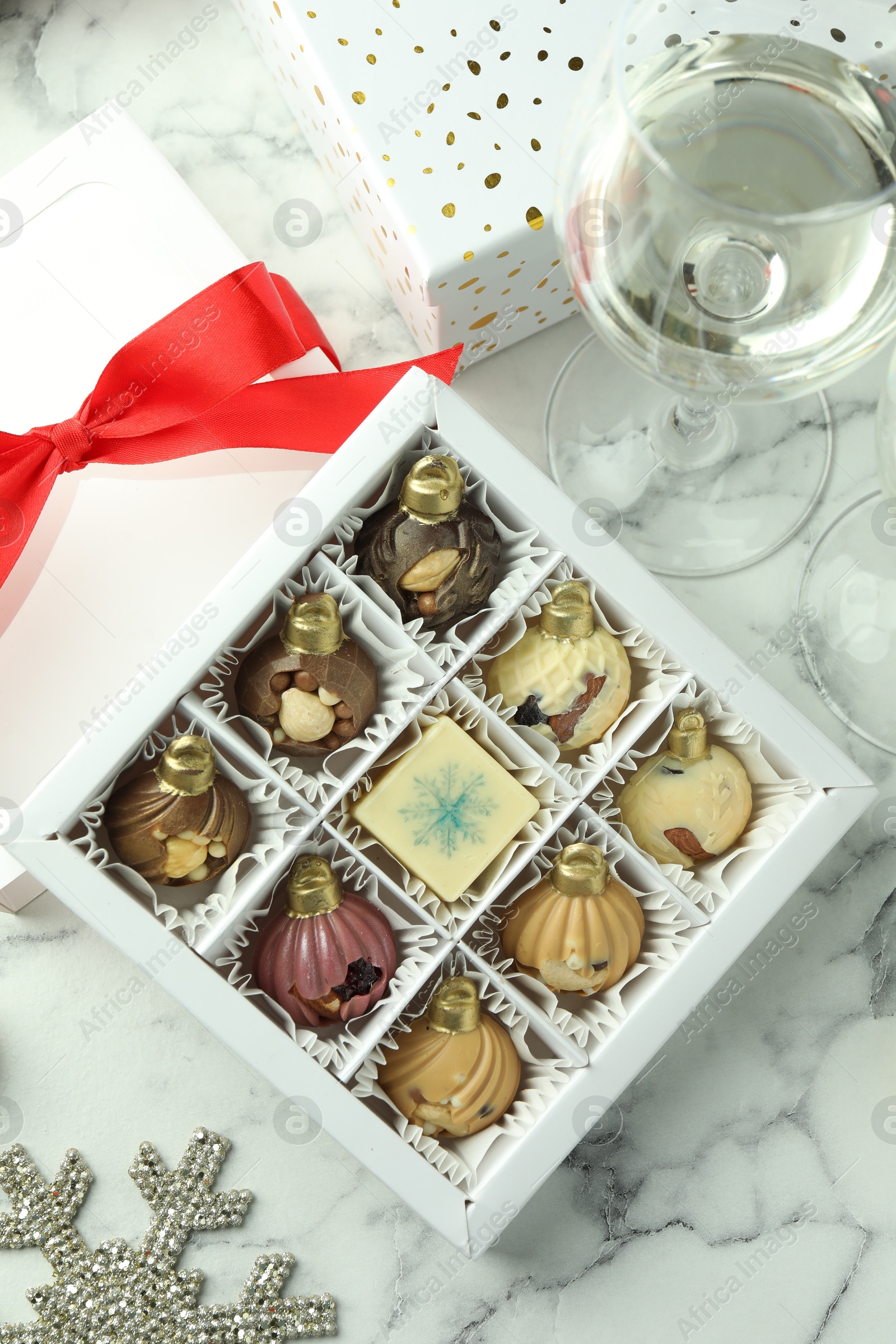 Photo of Box with tasty sweets in shape of baubles, wine and Christmas decor on white marble background, flat lay