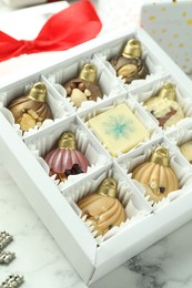 Photo of Box with tasty sweets in shape of baubles on white marble background, closeup