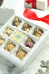 Photo of Box with tasty sweets in shape of baubles on white marble background, closeup