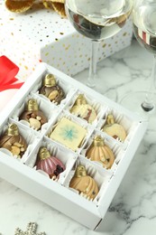 Photo of Box with tasty sweets in shape of baubles and wine on white marble background, closeup