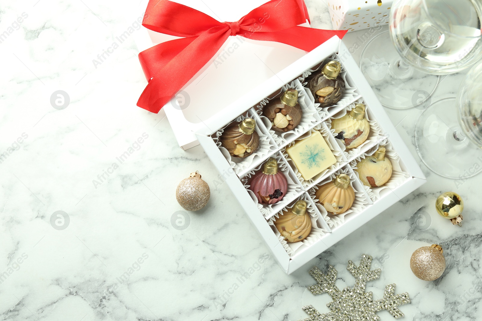 Photo of Box with tasty sweets in shape of baubles, wine and Christmas decor on white marble background, flat lay. Space for text