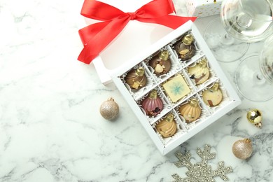 Photo of Box with tasty sweets in shape of baubles, wine and Christmas decor on white marble background, flat lay. Space for text