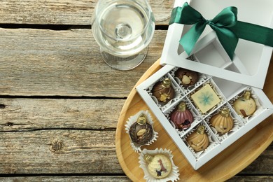 Photo of Box with tasty sweets in shape of baubles and wine on wooden background, flat lay. Space for text