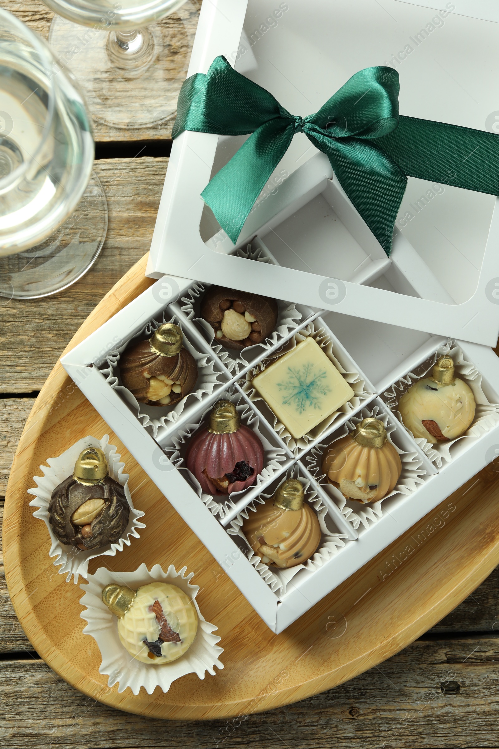 Photo of Box with tasty sweets in shape of baubles and wine on wooden background, flat lay