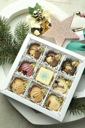 Photo of Box with tasty sweets in shape of baubles and Christmas decor on light background, closeup