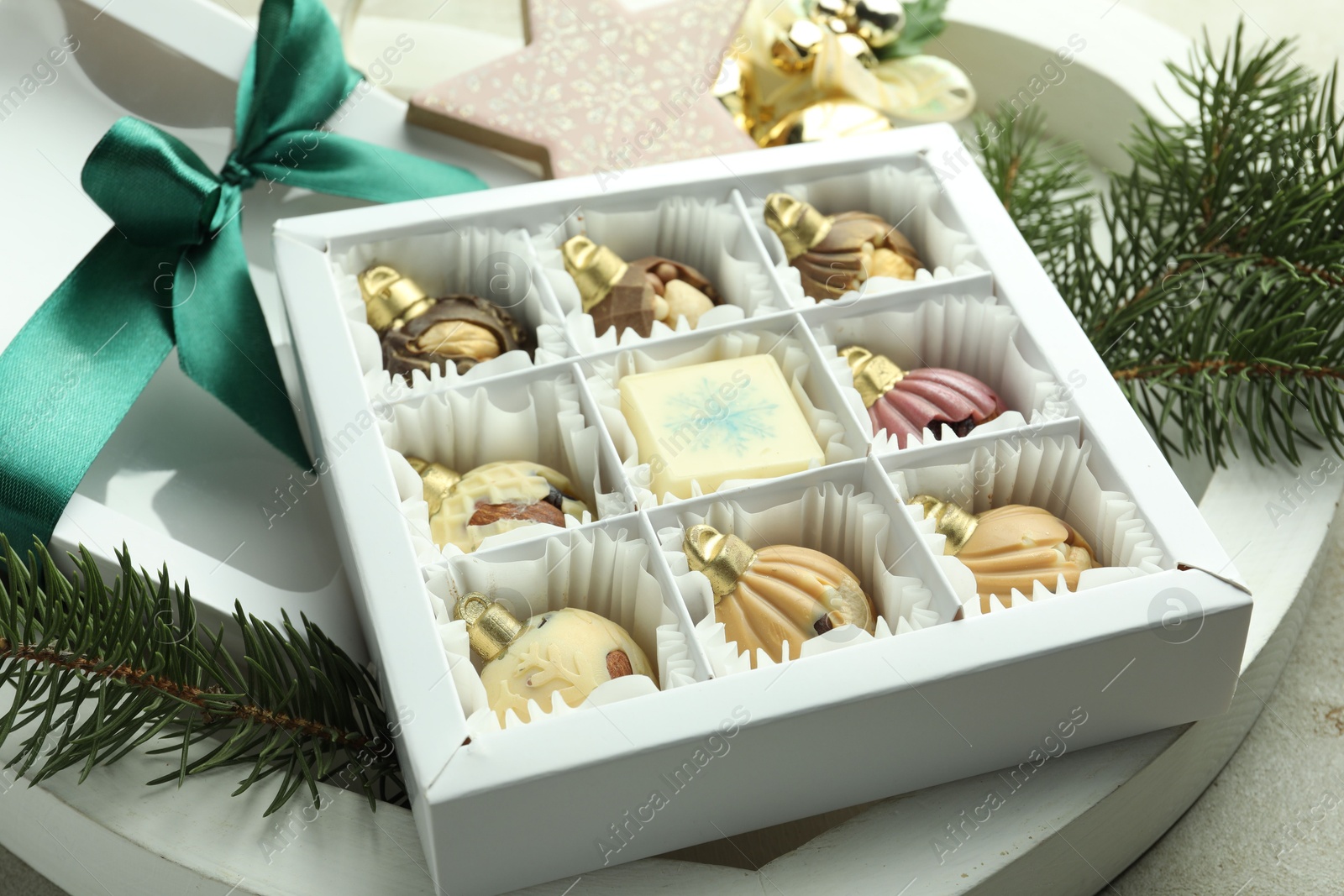 Photo of Box with tasty sweets in shape of baubles and Christmas decor on light background, closeup