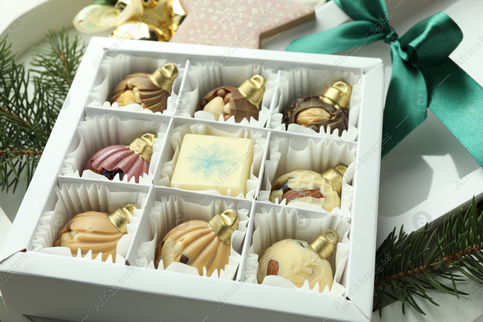 Photo of Box with tasty sweets in shape of baubles and Christmas decor on light background, closeup