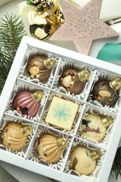 Photo of Box with tasty sweets in shape of baubles and Christmas decor on light background, closeup