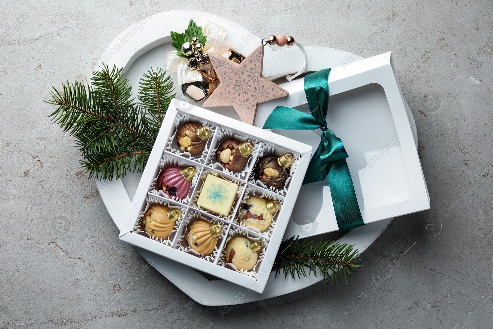 Photo of Box with tasty sweets in shape of baubles and Christmas decor on grey background, top view